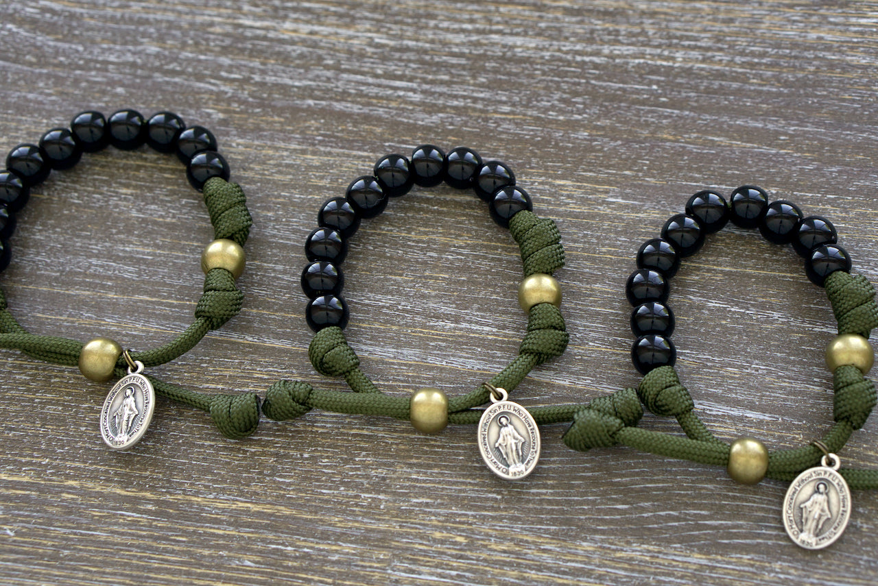 Army Green and Black Kid's Rosary Bracelet featuring durable paracord, black acrylic beads for Hail Mary prayers, olive Our Father bead, and a Miraculous Medal.