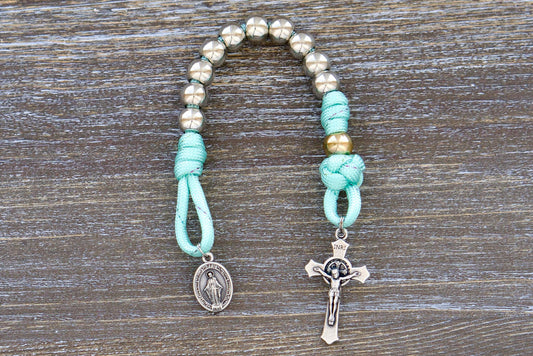 A single decade paracord rosary with 10mm acrylic beads, silver Hail Mary beads, a rose gold Our Father bead, a miniature St. Benedict crucifix, and a Miraculous Medal. Designed for children, it features durable paracord, perfect for backpacks or pockets