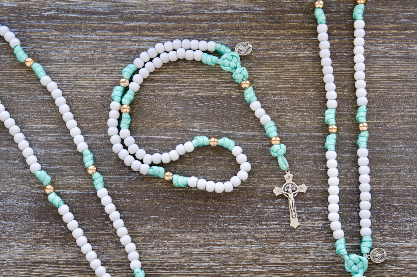 A child-sized mint green and white paracord rosary featuring durable 10mm acrylic beads, a smaller Miraculous Medal, and a 2-inch St. Benedict crucifix. Ideal for First Communion or Easter gifts, promoting prayer and faith in young children.