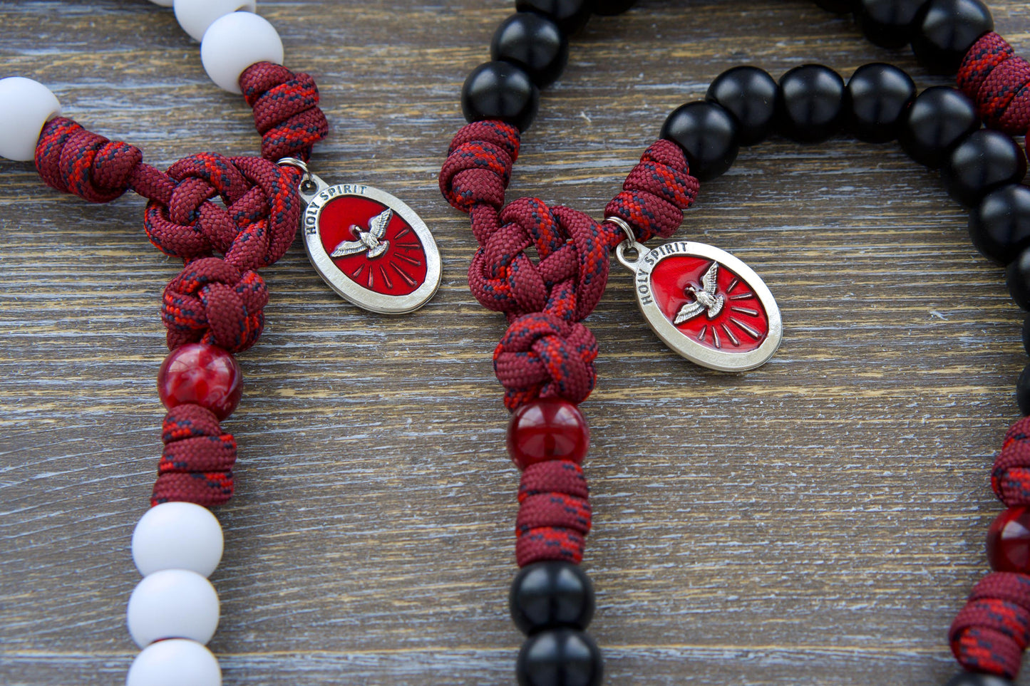 Vibrant maroon paracord rosary, "Crimson Shield," featuring black or white Hail Mary beads, a gleaming black or white enamel St. Benedict crucifix, and a red Holy Spirit medal.