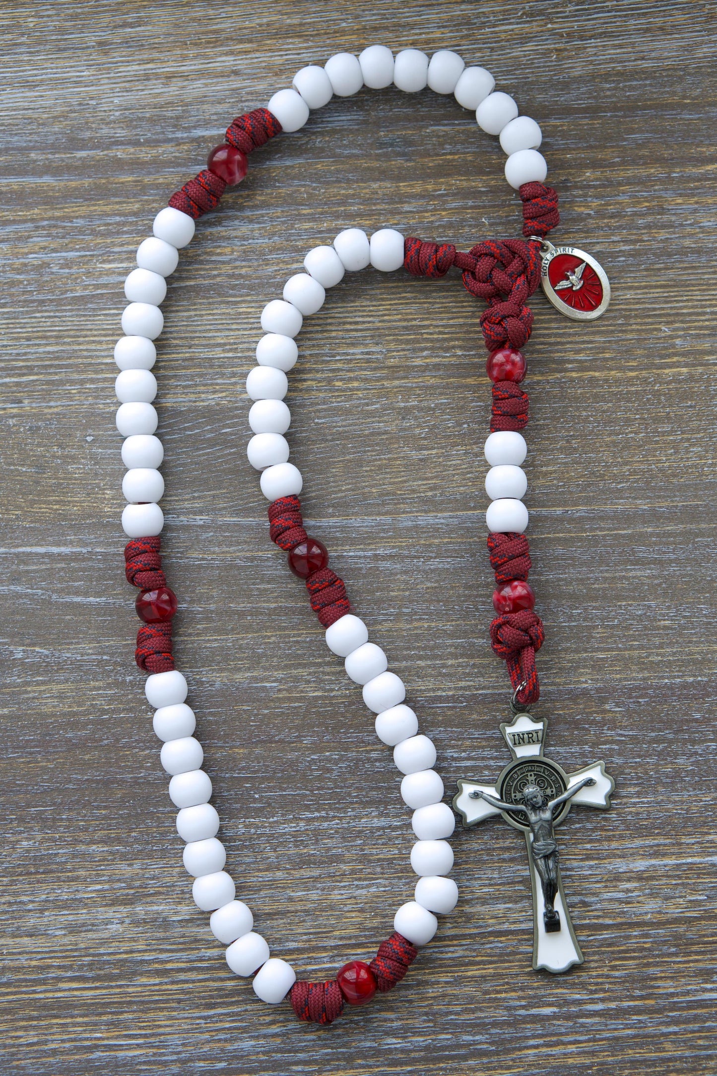 Crimson Shield Rosary: A handmade, five-decade paracord rosary featuring maroon red cord, black or white Hail Mary beads, a gleaming black (or white) St. Benedict crucifix, and a vibrant red Holy Spirit medal.