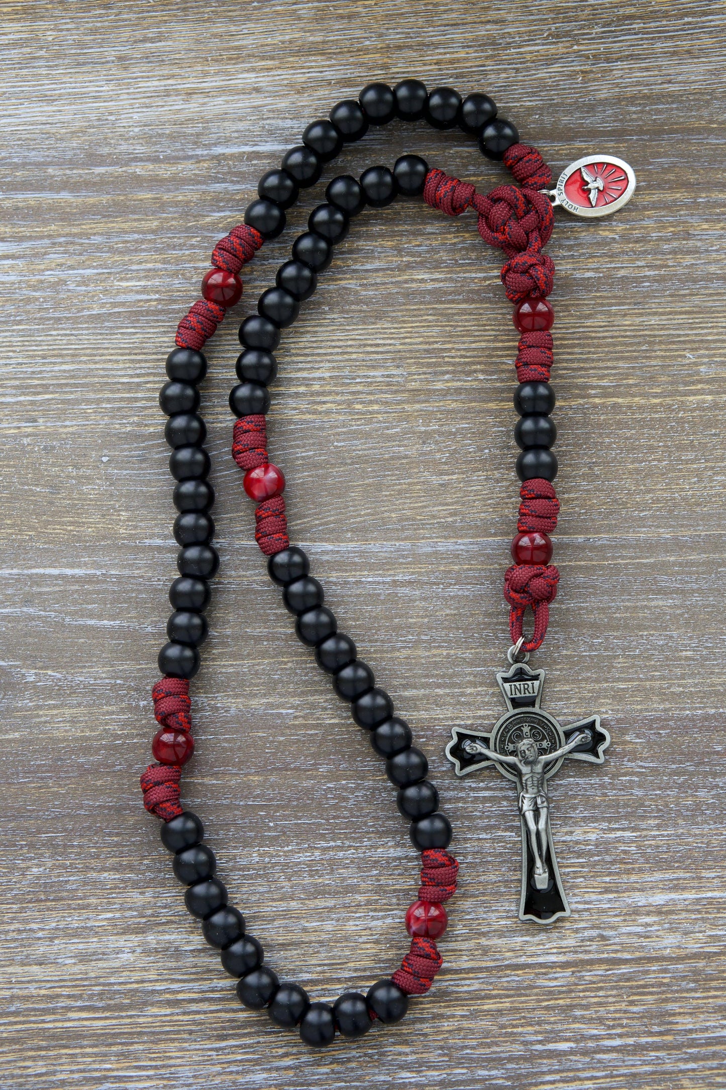 Crimson Shield Rosary: A handcrafted 5-decade paracord rosary in maroon red, featuring black or white Hail Mary beads, a gleaming black (or white) enamel St. Benedict crucifix, and a vibrant red Holy Spirit devotional medal.