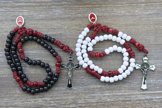 A vibrant maroon red paracord rosary, "The Crimson Shield," featuring black (or white) Hail Mary beads and a gleaming black (or white) enamel St. Benedict crucifix.