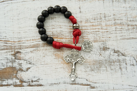 The Defender of Faith pocket rosary features matte black beads, red paracord, a silver crucifix, and St. Benedict medal.
