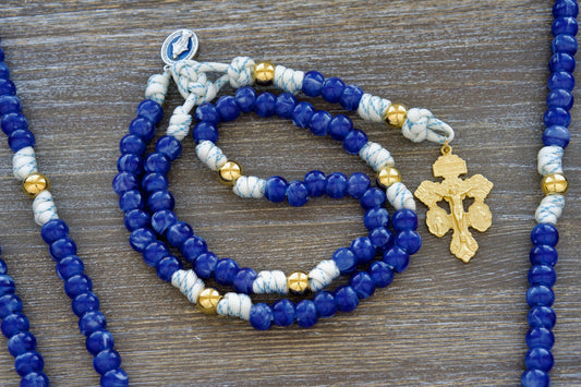 5 Decade Paracord Rosary: White paracord infused with blue accents, featuring radiant gold Our Father beads, unique blue acrylic Hail Mary beads, and a blue enamel Miraculous Medal.  A striking gold crucifix completes this luminous rosary, ideal for prayer and spiritual devotion.