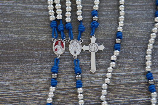 A handcrafted premium paracord rosary featuring royal blue paracord, silver and gunmetal alloy beads, and a detailed red enamel Divine Mercy centerpiece engraved with "Jesus I Trust in You" and Saint Faustina's image. Includes a 2-inch St. Benedict crucifix. Inspired by the devotion to Divine Mercy.