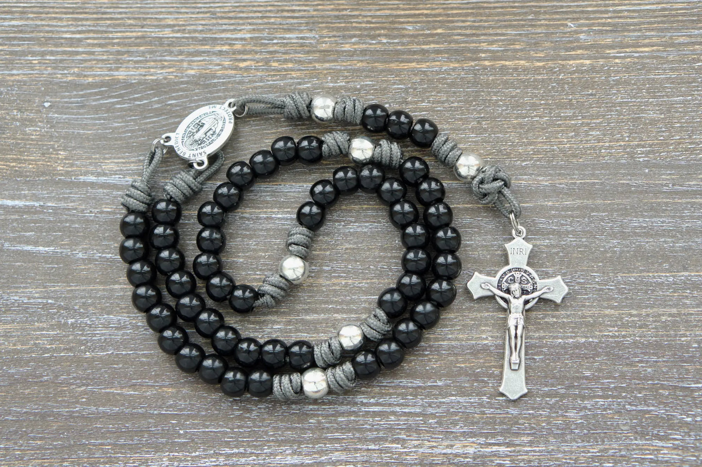 Silver Our Father beads and a St. Benedict crucifix adorn a durable black paracord rosary with 10mm metal alloy Hail Mary beads.