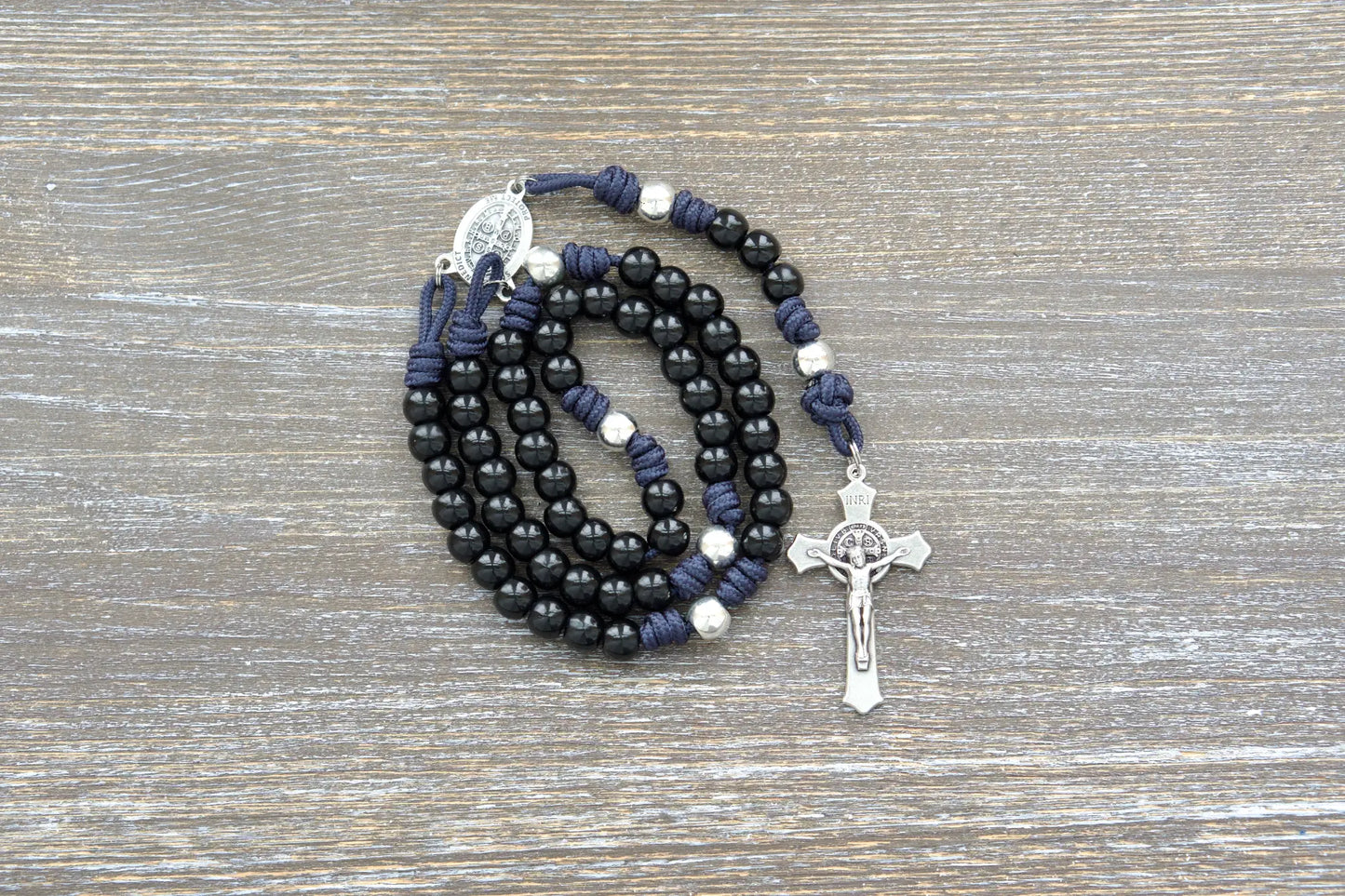 Sturdy navy blue paracord rosary with contrasting silver Our Father beads and black Hail Mary beads, featuring a St. Benedict medal centerpiece and crucifix.