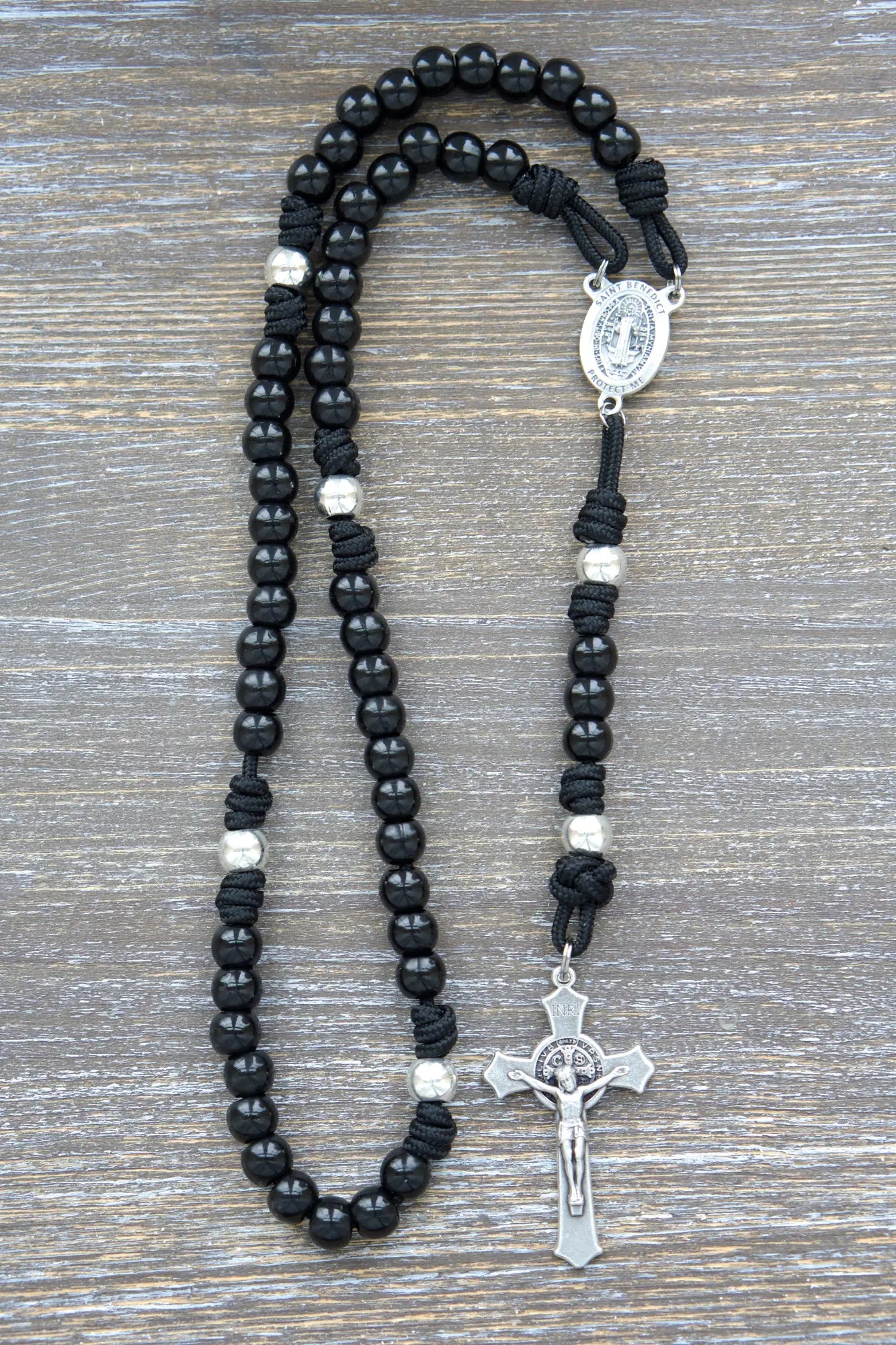 Silver Our Father beads and black metal alloy Hail Mary beads on a sturdy midnight black paracord rosary with a St. Benedict crucifix.