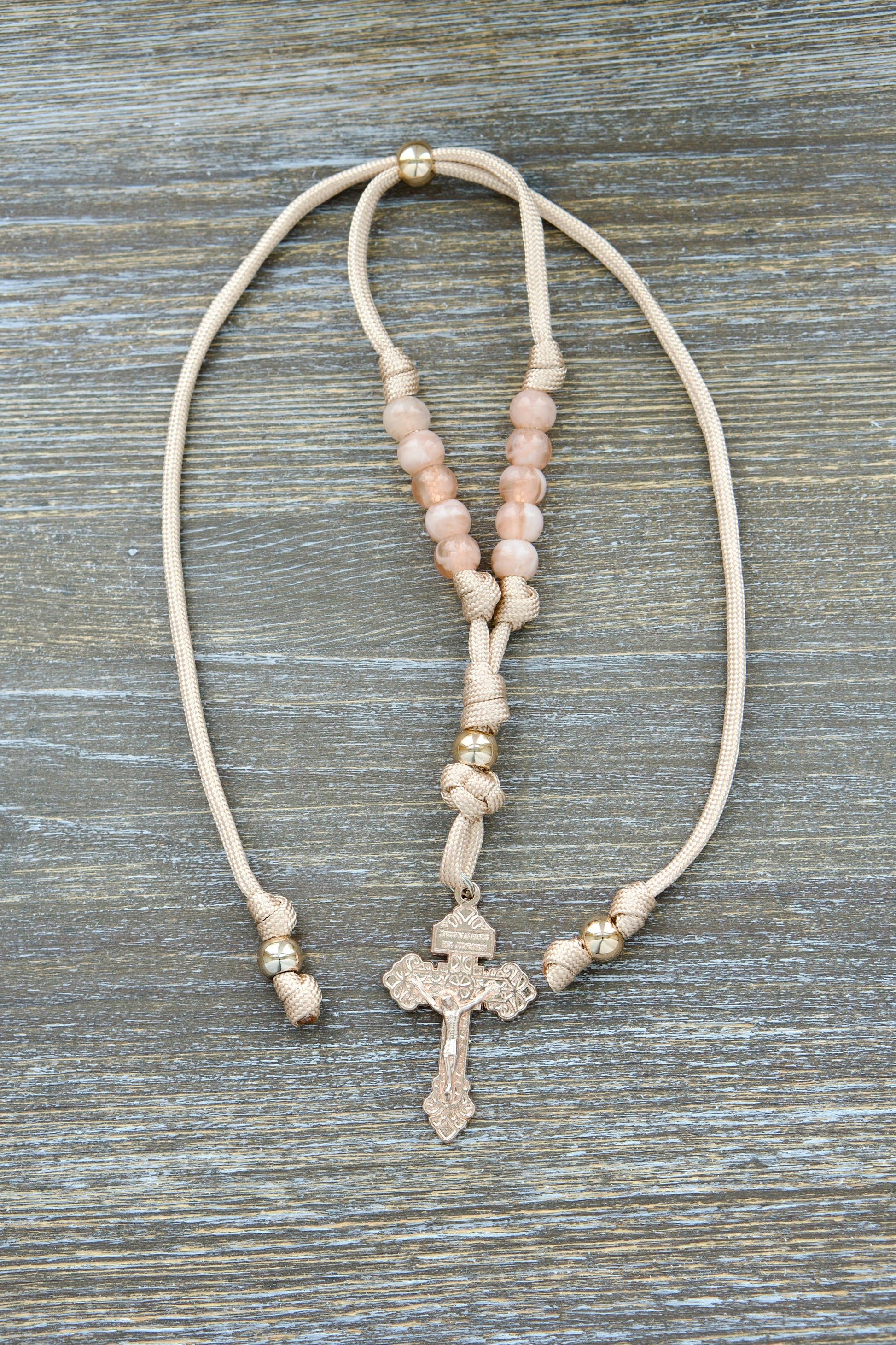 Handmade tan and rose-gold paracord rearview mirror rosary featuring a unique rose gold Pardon Crucifix centerpiece, milky pink Hail Mary beads, and a striking rose gold Our Father bead.