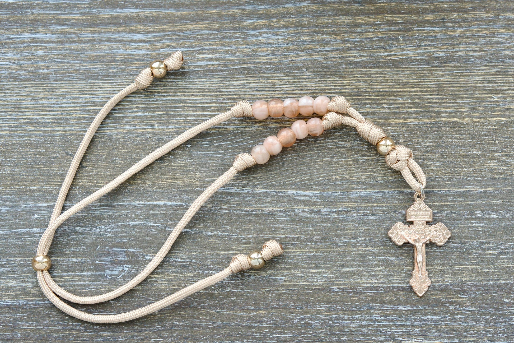 Tan and rose gold paracord Rosary hanging from a car rearview mirror. Features a rose gold Our Father bead, milky pink Hail Mary beads, and a unique rose gold Pardon Crucifix centerpiece.