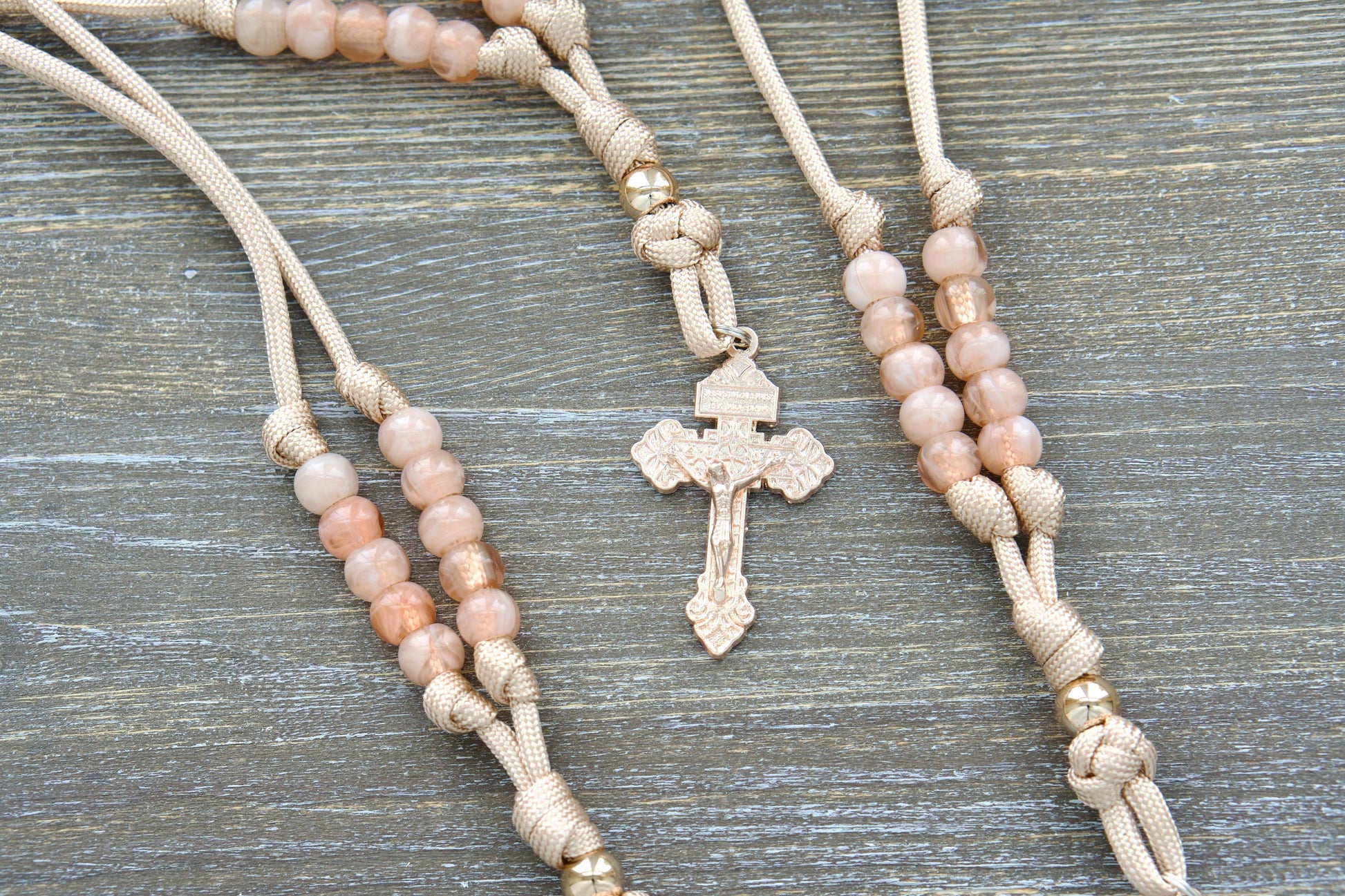 Gate of Heaven Rearview Mirror Rosary: Handmade tan and rose gold paracord rosary with a unique rose gold Pardon Crucifix centerpiece, featuring milky pink Hail Mary beads and a striking rose gold Our Father bead.