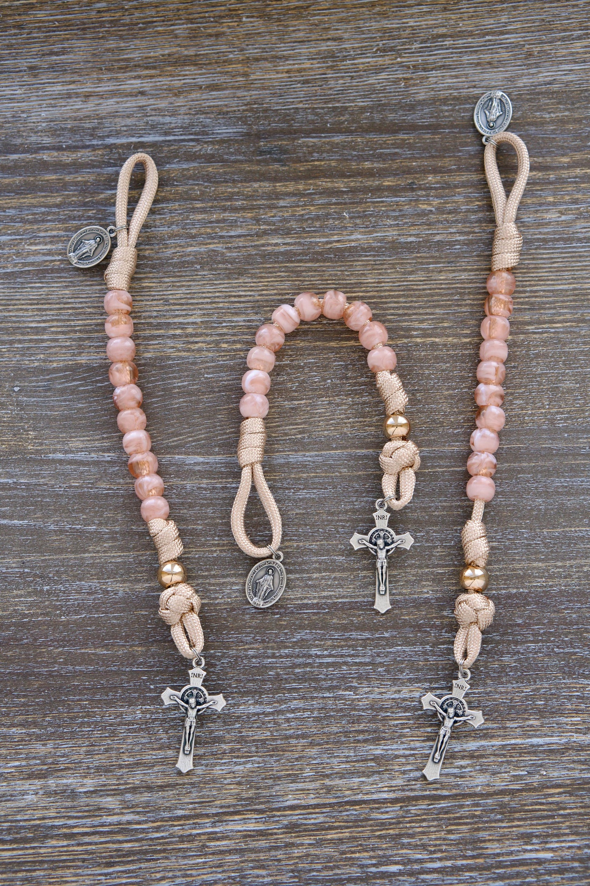 Gate of Heaven - Pocket Paracord Rosary: Close-up image showcasing rose-gold, tan, and milky pink paracord intertwined with 10mm acrylic Hail Mary beads and a shiny gold Our Father bead.