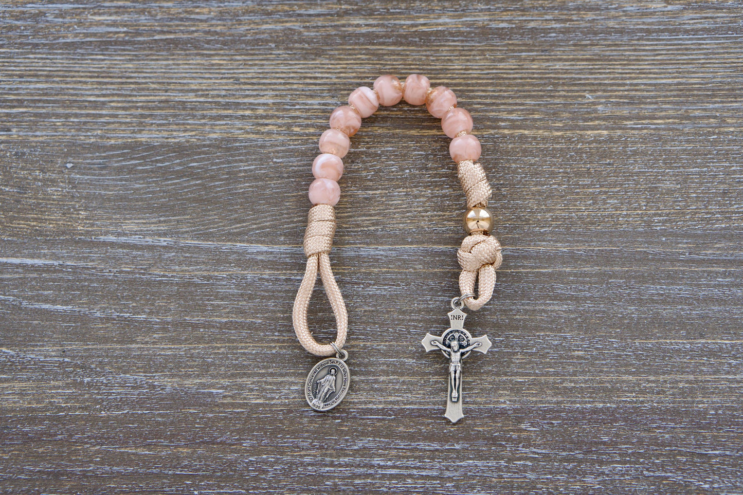 Gate of Heaven Pocket Paracord Rosary: A close-up image showcasing a miniature paracord rosary with rose-gold/tan paracord, milky pink Hail Mary beads, and a shiny gold Our Father bead.