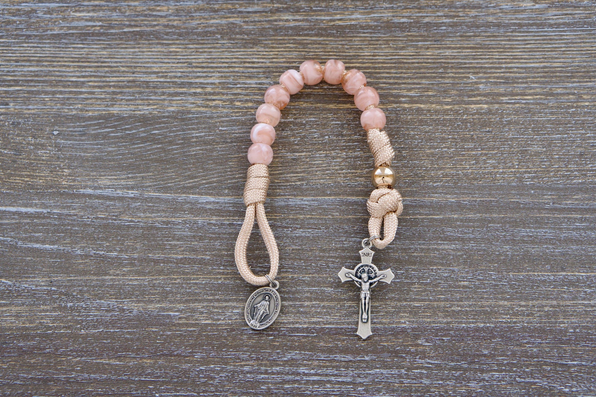 Gate of Heaven Pocket Paracord Rosary: A close-up image showcasing a miniature paracord rosary with rose-gold/tan paracord, milky pink Hail Mary beads, and a shiny gold Our Father bead.