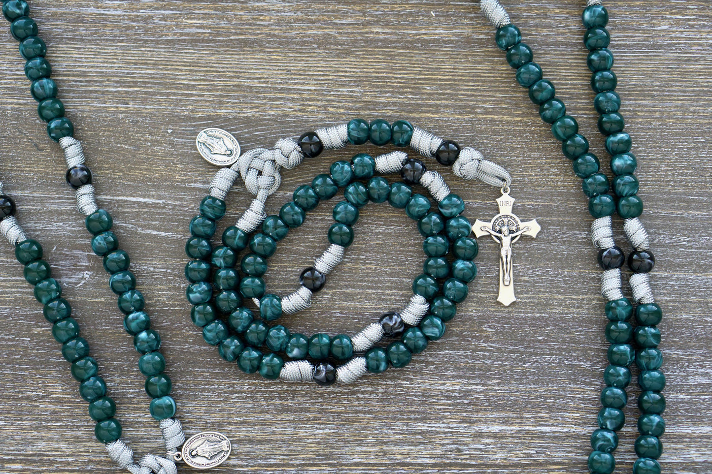 A vibrant Gemstone Colored 5 Decade Paracord Rosary featuring four stunning gemstone color options - Garnet Red, Ingolite Blue, Emerald Green, and Magenta. The rosary includes a standard 2" St. Benedict Crucifix for added protection and a Miraculous Medal devotional medal.