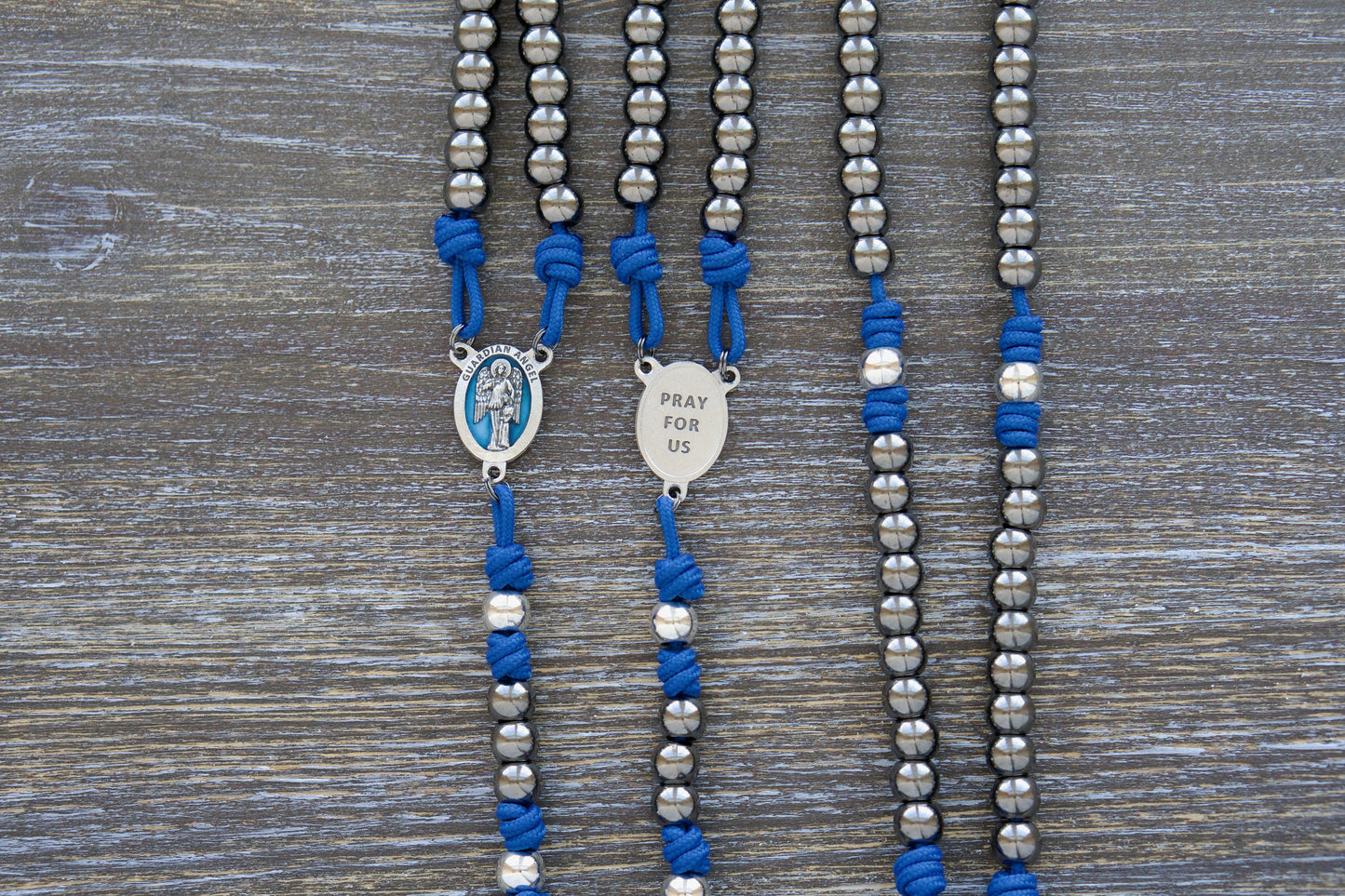 Guardian of Grace Premium Metal Paracord Rosary featuring royal blue paracord, gunmetal and silver metal alloy Hail Mary and Our Father beads, and a detailed blue enamel Guardian Angel centerpiece.