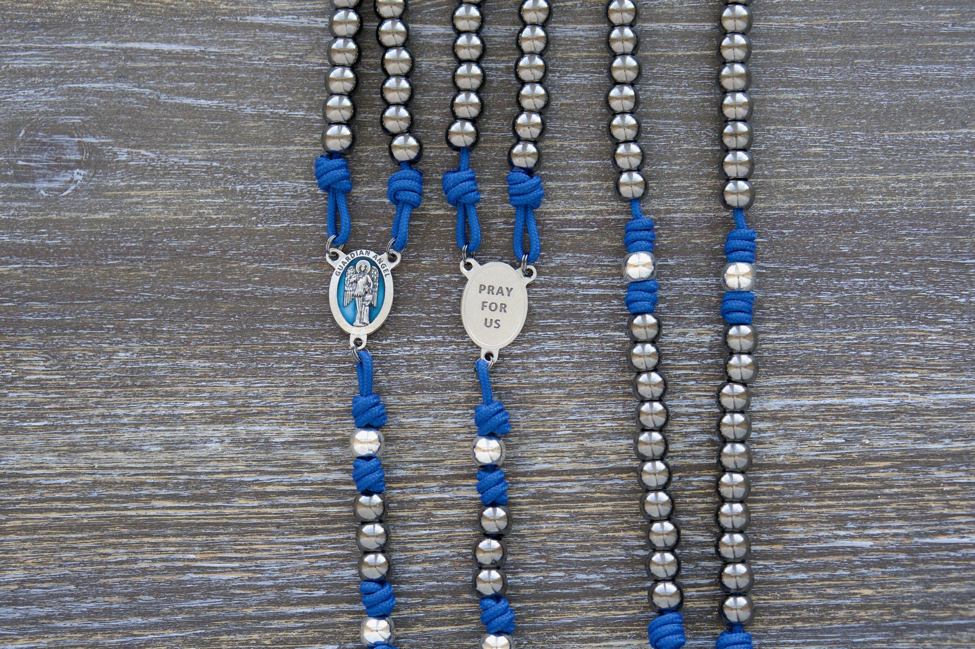 Guardian of Grace Premium Metal Paracord Rosary featuring royal blue paracord, gunmetal and silver metal alloy Hail Mary and Our Father beads, and a detailed blue enamel Guardian Angel centerpiece.