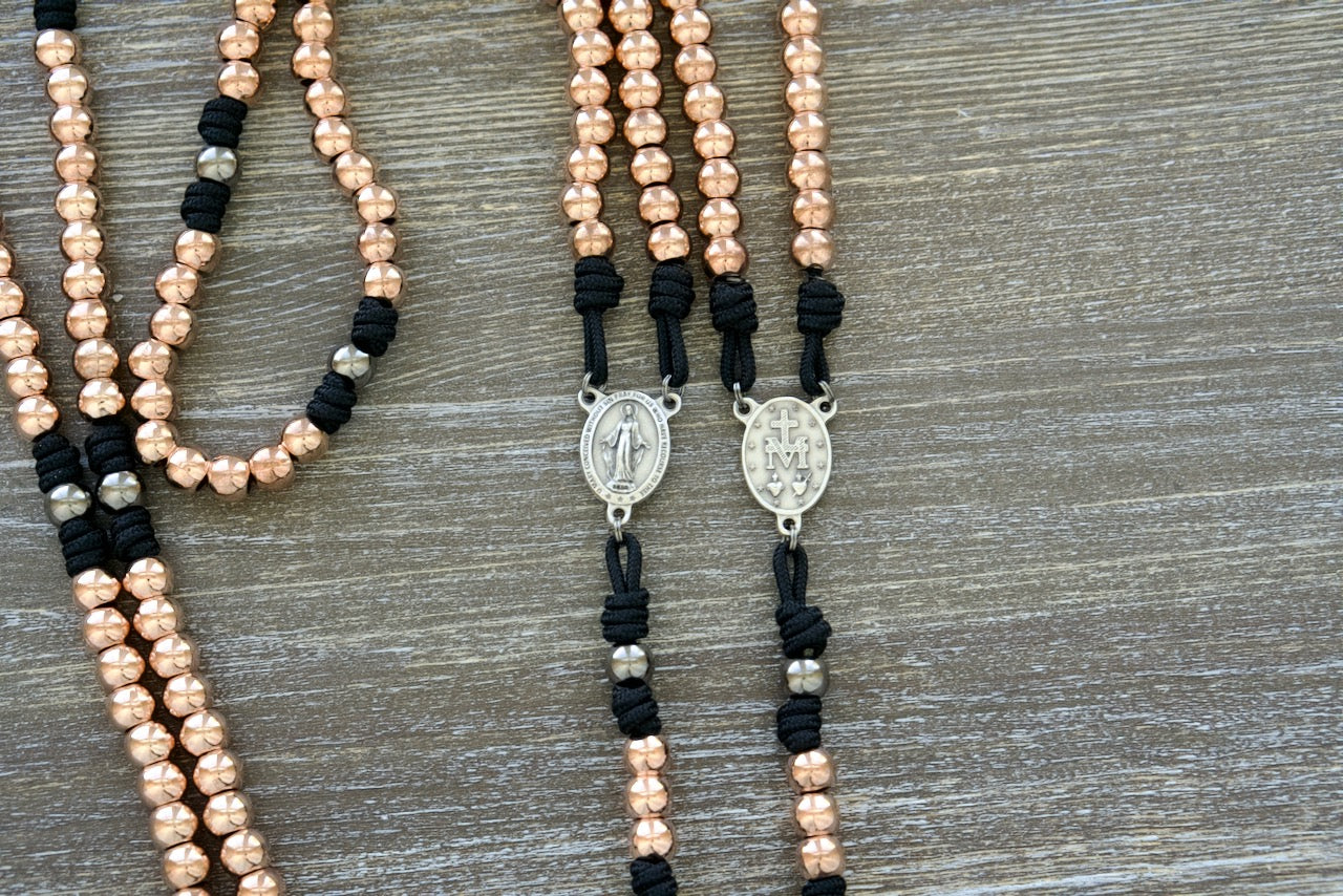 Immaculate Strength | Rose Gold, Black and Gunmetal Premium Metal Rosary: A stunning, durable, and unbreakable paracord rosary designed for women seeking spiritual strength and guidance. Features rose-gold Hail Mary beads, gunmetal Our Father beads, a silver Miraculous Medal centerpiece, and a 2-inch St. Benedict crucifix.