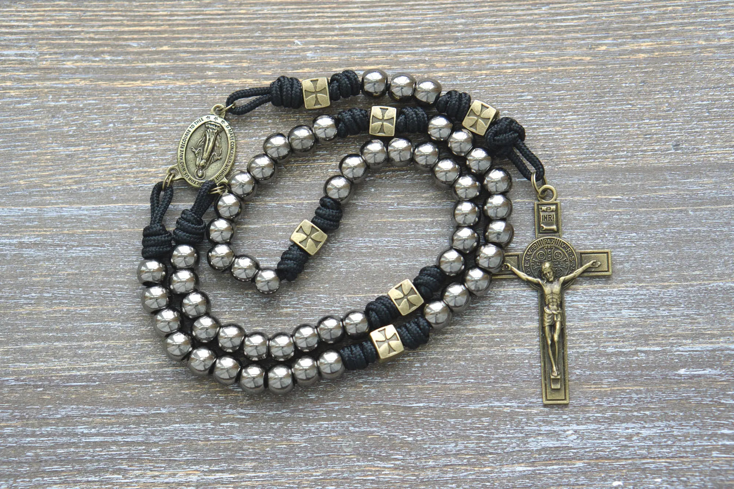 Black paracord rosary featuring olive Our Father beads, gunmetal Hail Mary beads, a Miraculous Medal centerpiece, and a St. Benedict crucifix.