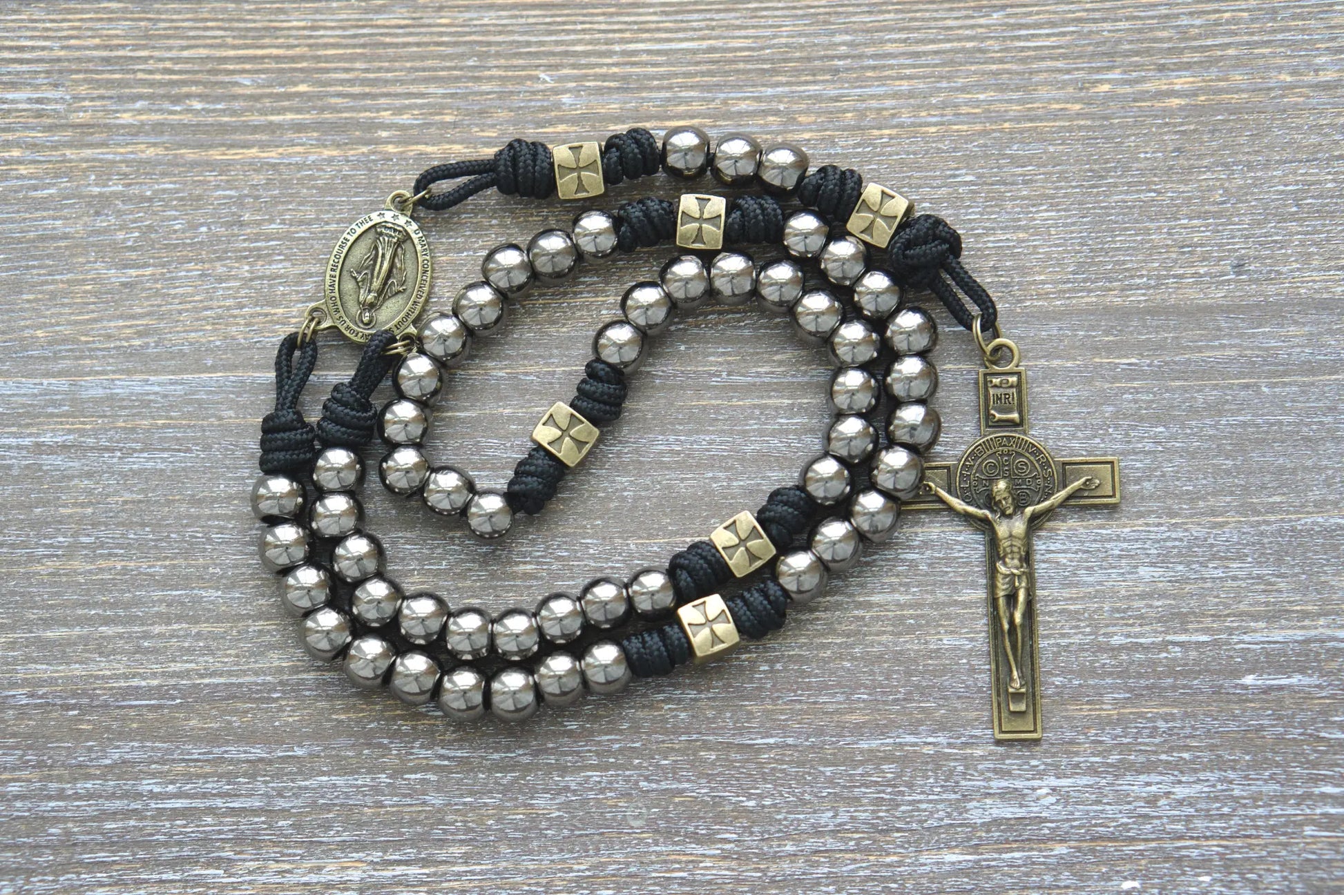 Black paracord rosary featuring olive Our Father beads, gunmetal Hail Mary beads, a Miraculous Medal centerpiece, and a St. Benedict crucifix.