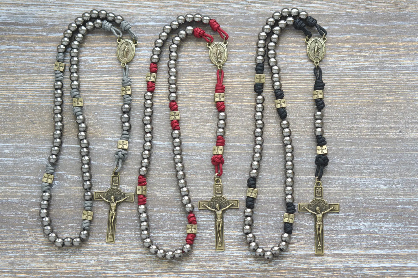 Three handcrafted paracord rosaries with olive crusader beads, gunmetal Hail Mary beads, a Miraculous Medal centerpiece, and a St. Benedict crucifix.