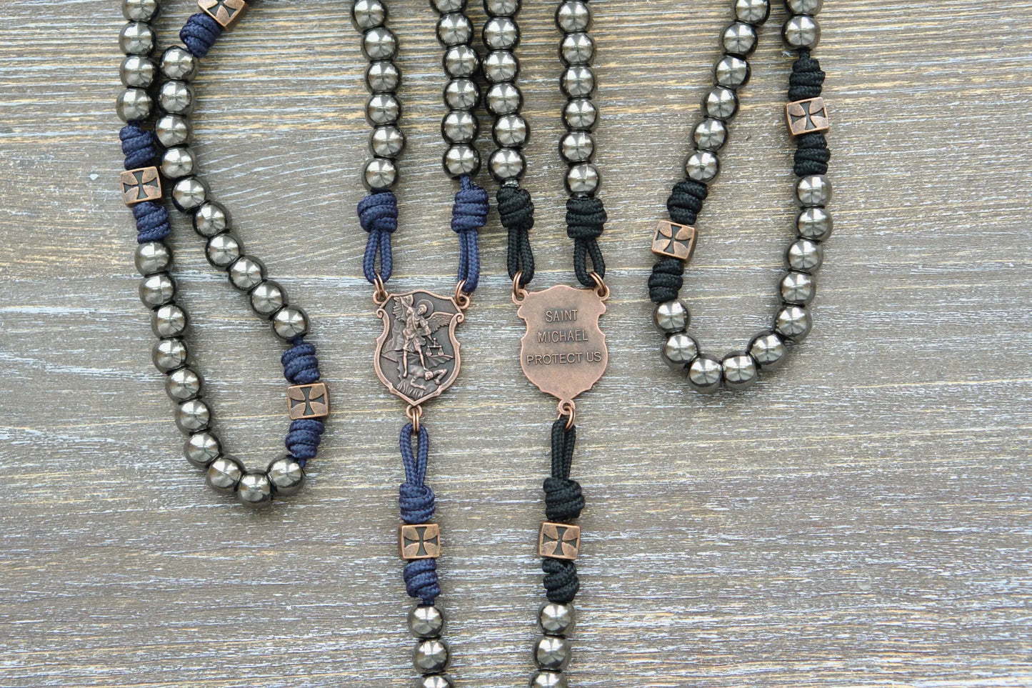 Black or navy blue paracord rosary featuring 10mm gunmetal Hail Mary beads, copper accents, and a St. Michael centerpiece medal.