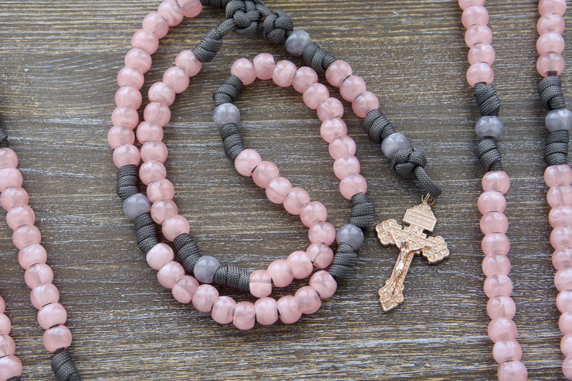 Ite Ad Joseph Paracord Rosary: A handcrafted, full-sized rosary featuring grey and milky pink paracord and beads, a rose gold Pardon Crucifix, and a St. Joseph devotional medal.