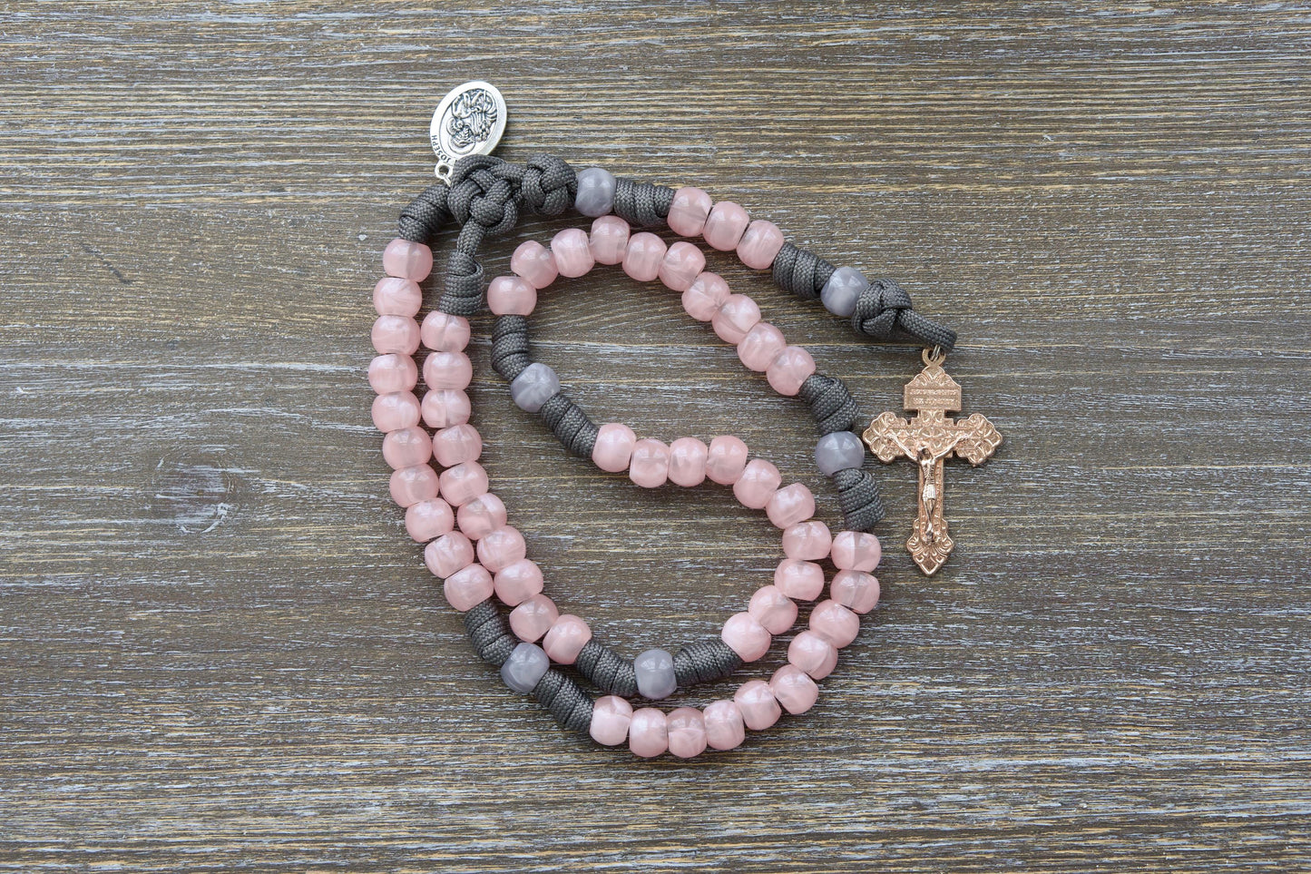 Ite Ad Joseph Paracord Rosary: A handcrafted, full-sized rosary featuring grey and milky pink colors and a radiant rose gold Pardon Crucifix