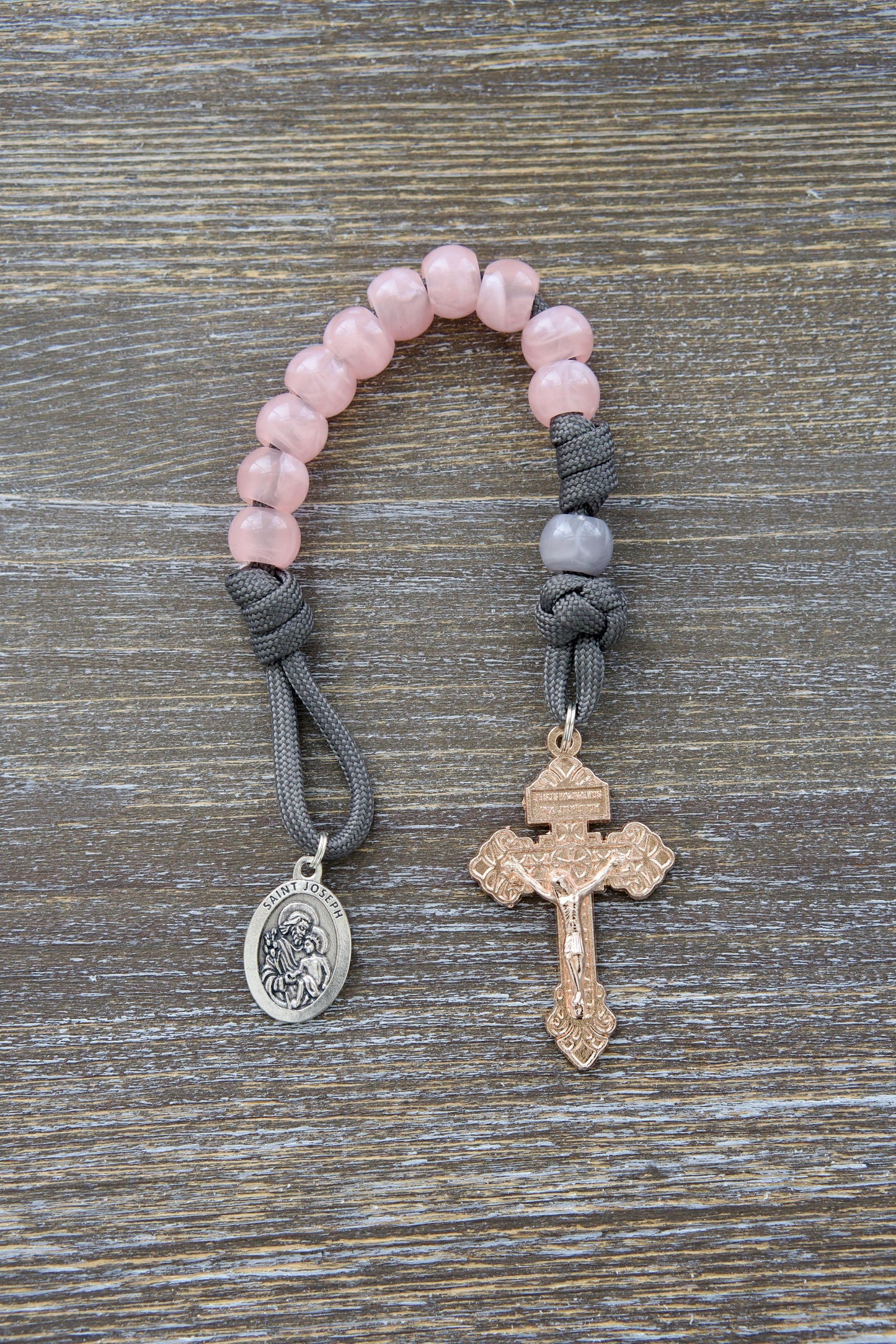 A stylish grey paracord single decade rosary, the "Ite Ad Joseph" features milky grey Our Father beads and contrasting milky pink Hail Mary beads.