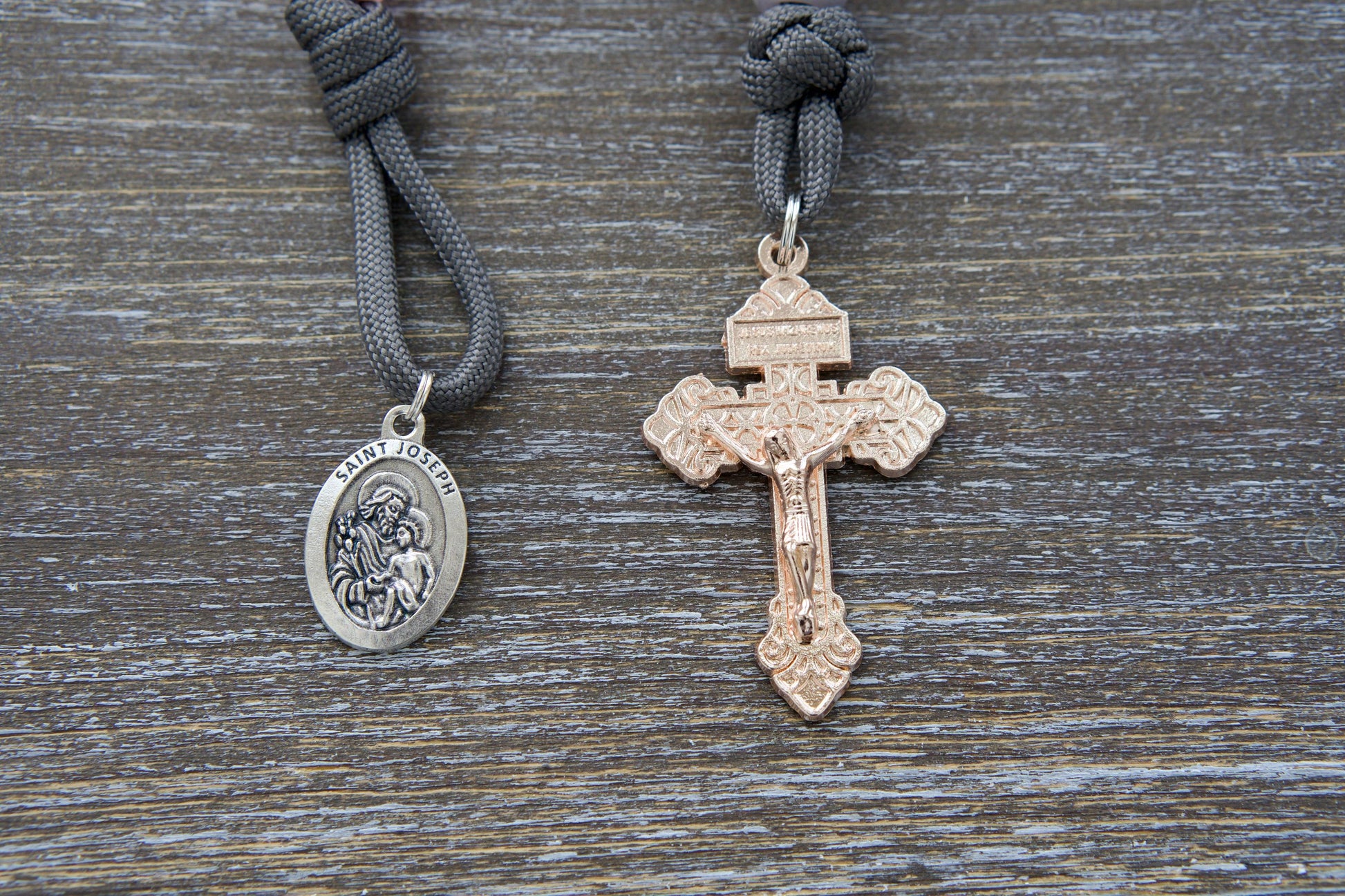 Pocket paracord rosary, "Ite Ad Joseph," featuring grey paracord, milky grey Our Father bead, contrasting milky pink Hail Mary beads, a rose gold Pardon Crucifix, and a St. Joseph devotional medal.