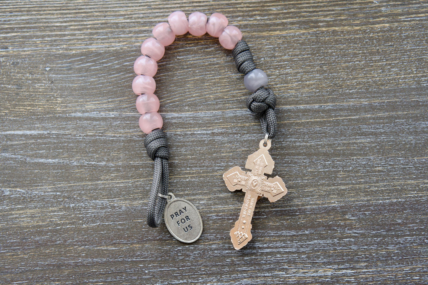 A durable grey paracord single-decade rosary, the "Ite Ad Joseph" rosary, features milky grey Our Father and contrasting pink Hail Mary beads.