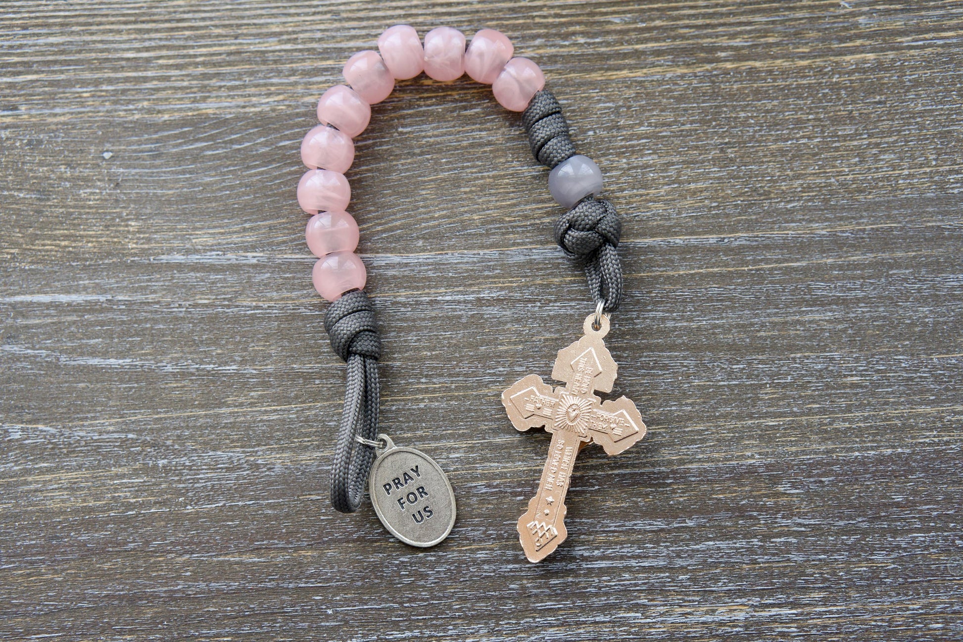 A durable grey paracord single-decade rosary, the "Ite Ad Joseph" rosary, features milky grey Our Father and contrasting pink Hail Mary beads.