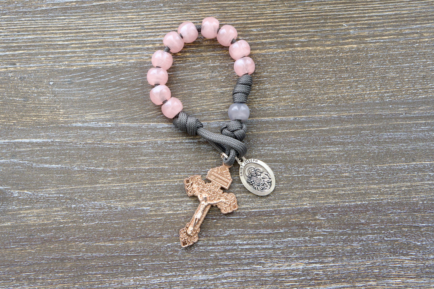 Ite Ad Joseph Pocket Paracord Rosary: A single decade, grey paracord rosary with milky grey Our Father bead, milky pink Hail Mary beads, a rose gold Pardon crucifix, and a St. Joseph devotional medal.