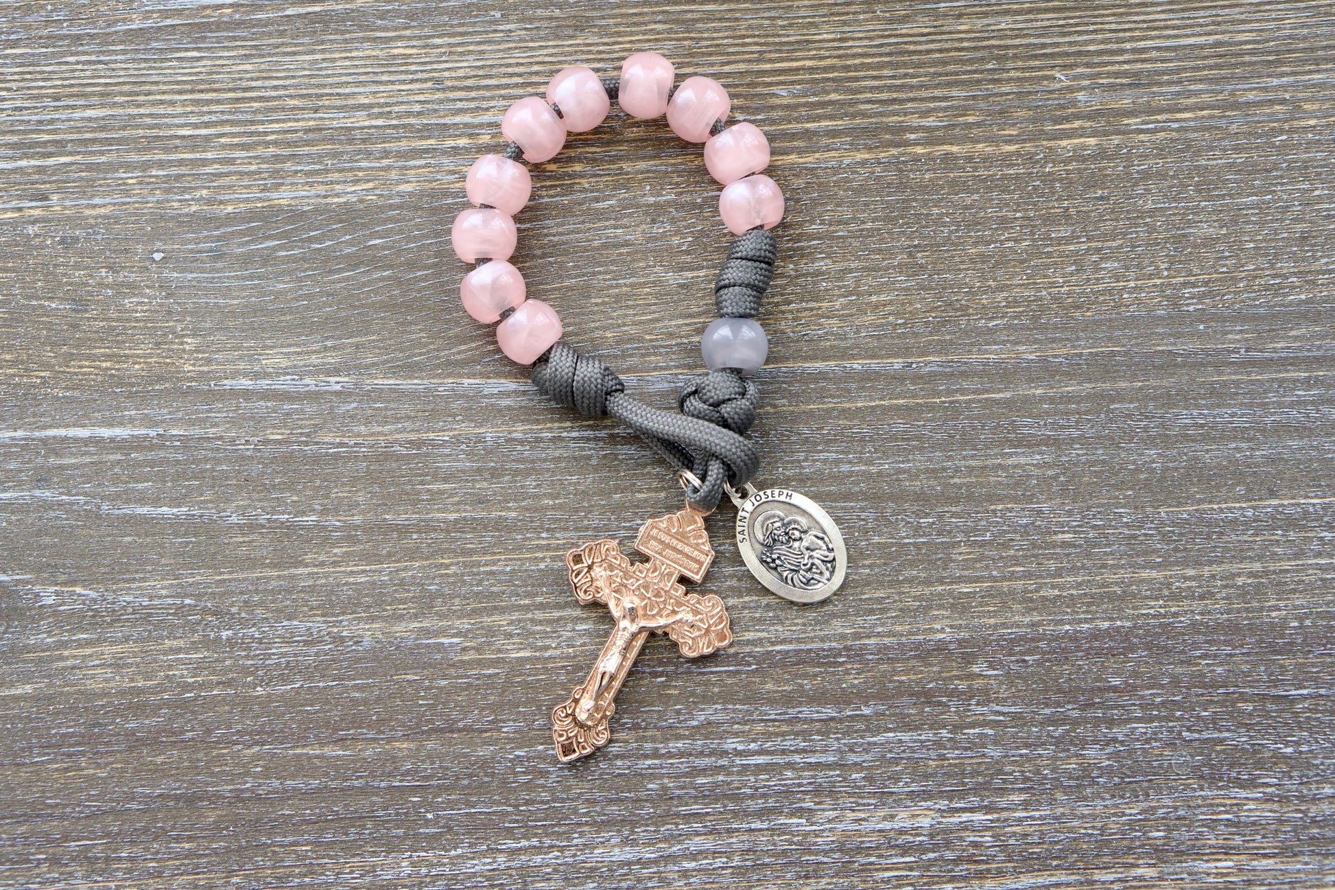 Ite Ad Joseph Pocket Paracord Rosary: A single decade, grey paracord rosary with milky grey Our Father bead, milky pink Hail Mary beads, a rose gold Pardon crucifix, and a St. Joseph devotional medal.