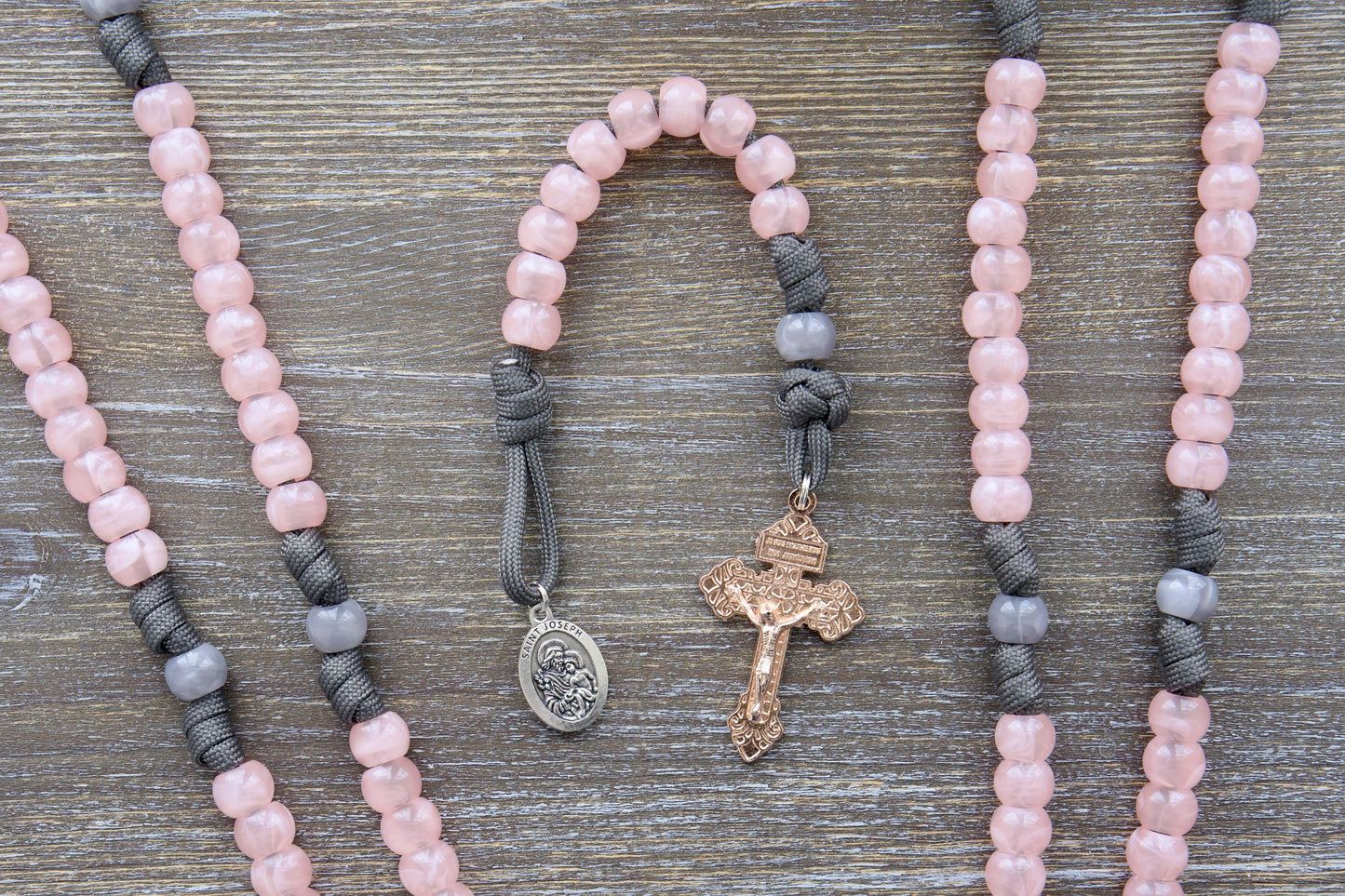 Elegant single-decade paracord rosary in grey and pink, featuring a milky grey Our Father bead, contrasting pink Hail Mary beads, a rose gold Pardon crucifix, and a St. Joseph devotional medal.