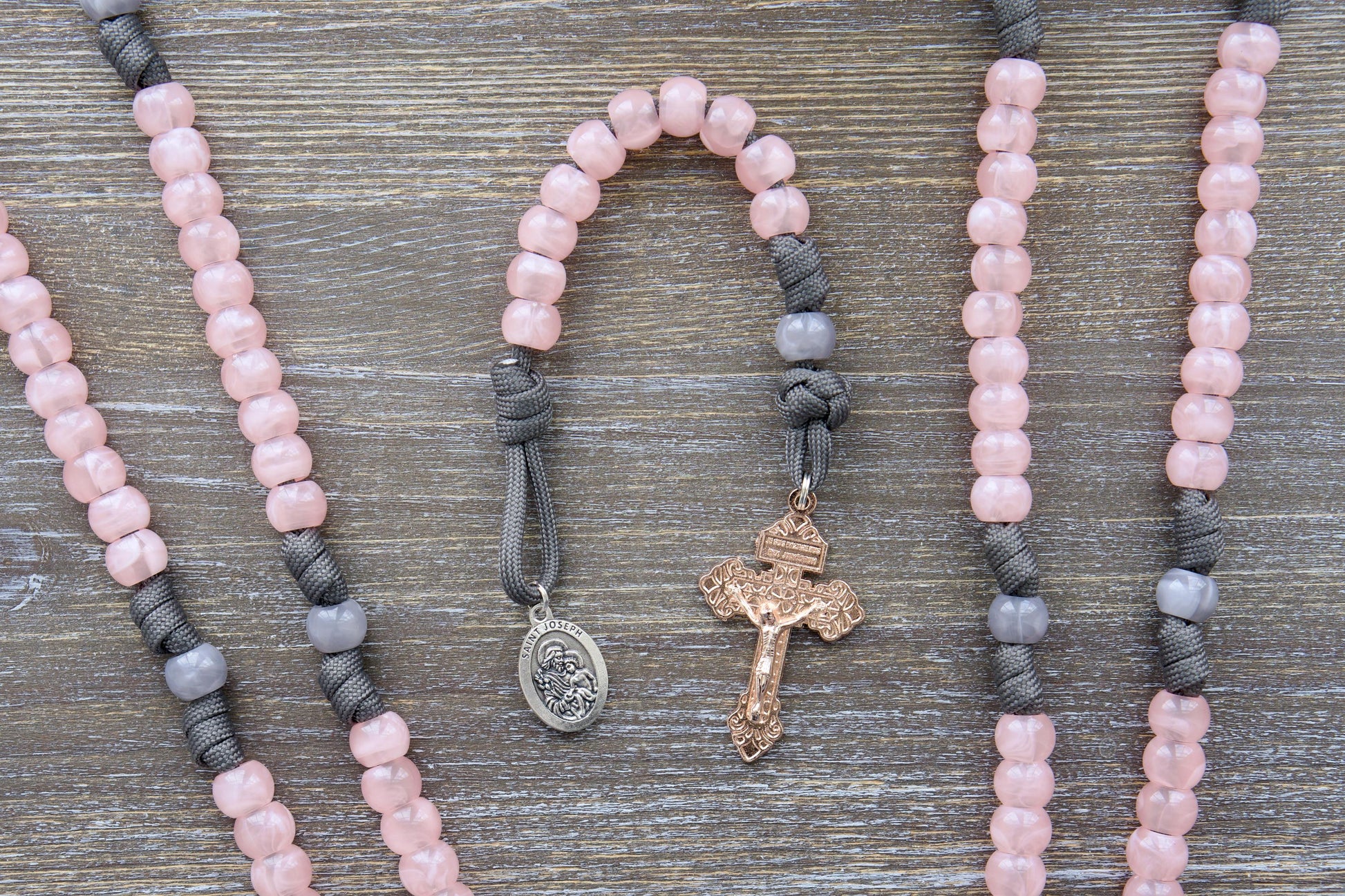Elegant single-decade paracord rosary in grey and pink, featuring a milky grey Our Father bead, contrasting pink Hail Mary beads, a rose gold Pardon crucifix, and a St. Joseph devotional medal.