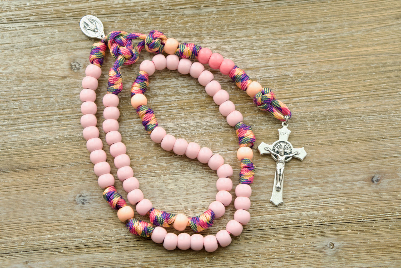 A colorful, fun, and durable kid's rosary designed for young girls, featuring light pink Hail Mary beads, a warm peach Our Father bead, and a smaller than normal Miraculous Medal. The unique pink camo paracord adds an adventurous touch to the design, perfect for little hands on-the-go.