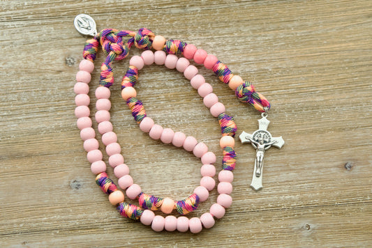 A colorful, fun, and durable kid's rosary designed for young girls, featuring light pink Hail Mary beads, a warm peach Our Father bead, and a smaller than normal Miraculous Medal. The unique pink camo paracord adds an adventurous touch to the design, perfect for little hands on-the-go.