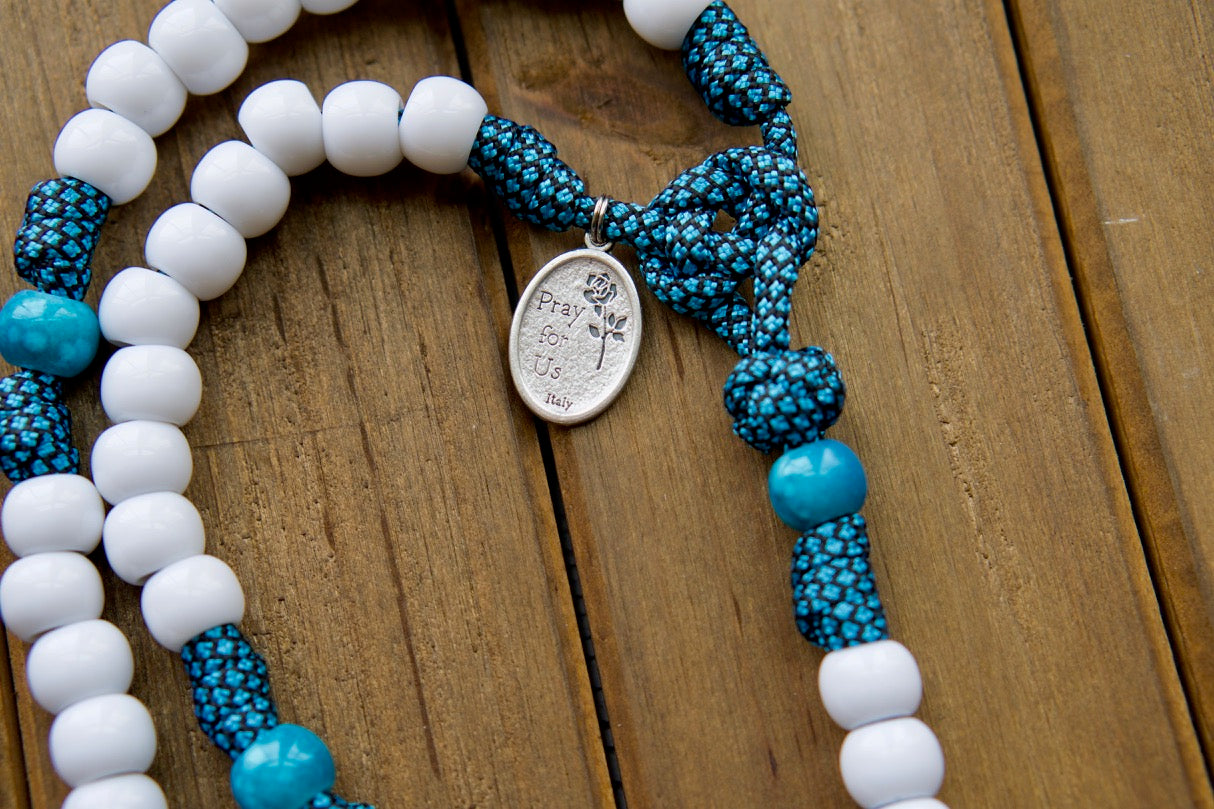 Our Lady of Perpetual Help - Turquoise - 5 Decade Paracord Rosary: A durable and unbreakable paracord rosary designed to withstand life's battles while remaining a powerful spiritual weapon. Featuring an exclusive Our Lady of Perpetual Help design, white Hail Mary beads, matching turquoise Our Father beads, and a large 3" white enamel St. Benedict Crucifix.