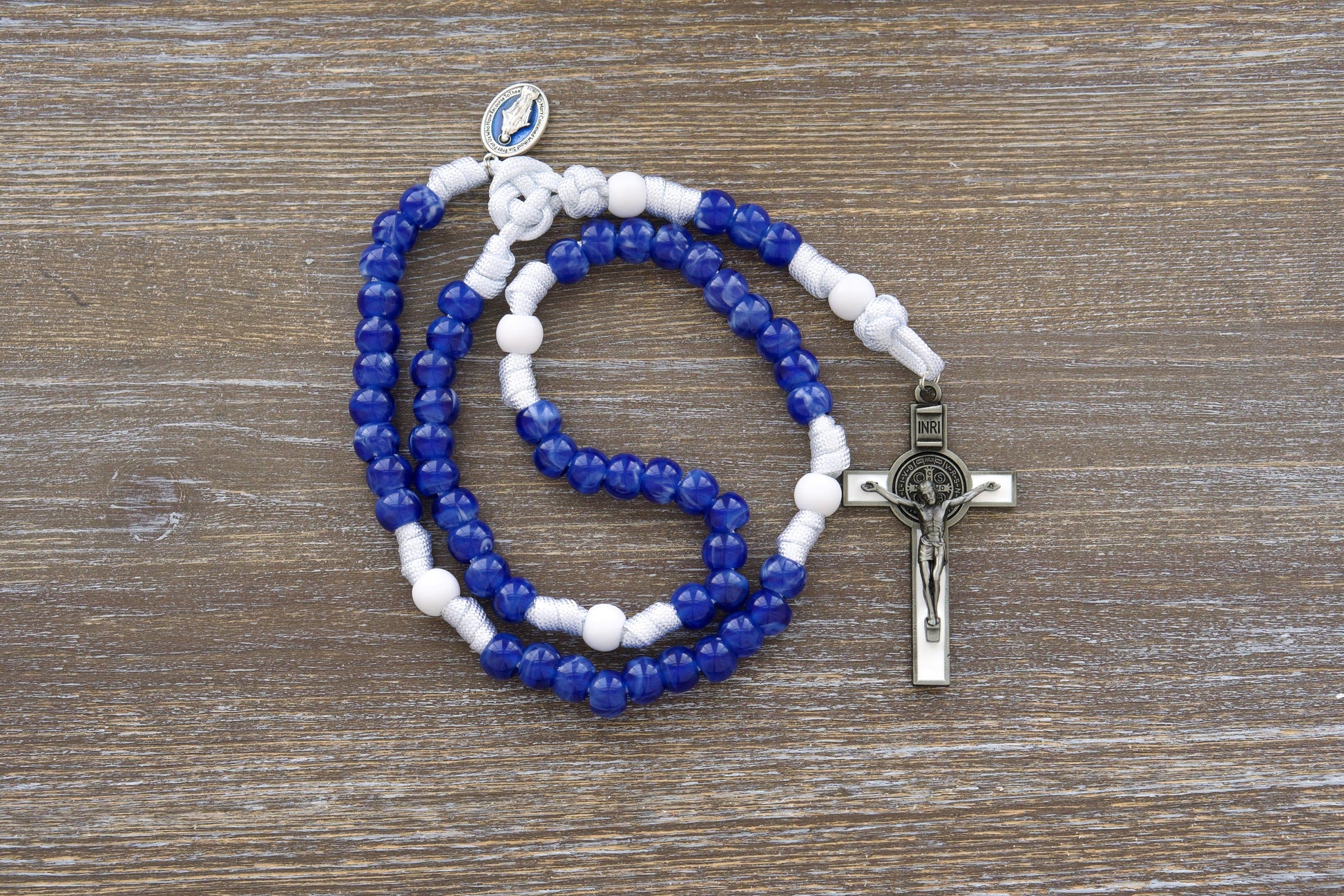 A handcrafted "Our Lady's Mantle" 5-decade paracord rosary featuring strong white paracord and a choice of two styles: one with a navy blue Miraculous Medal and the other with a striking silver-toned Miraculous Medal, both paired with a white enamel St. Benedict crucifix and matte white and milky blue acrylic beads.