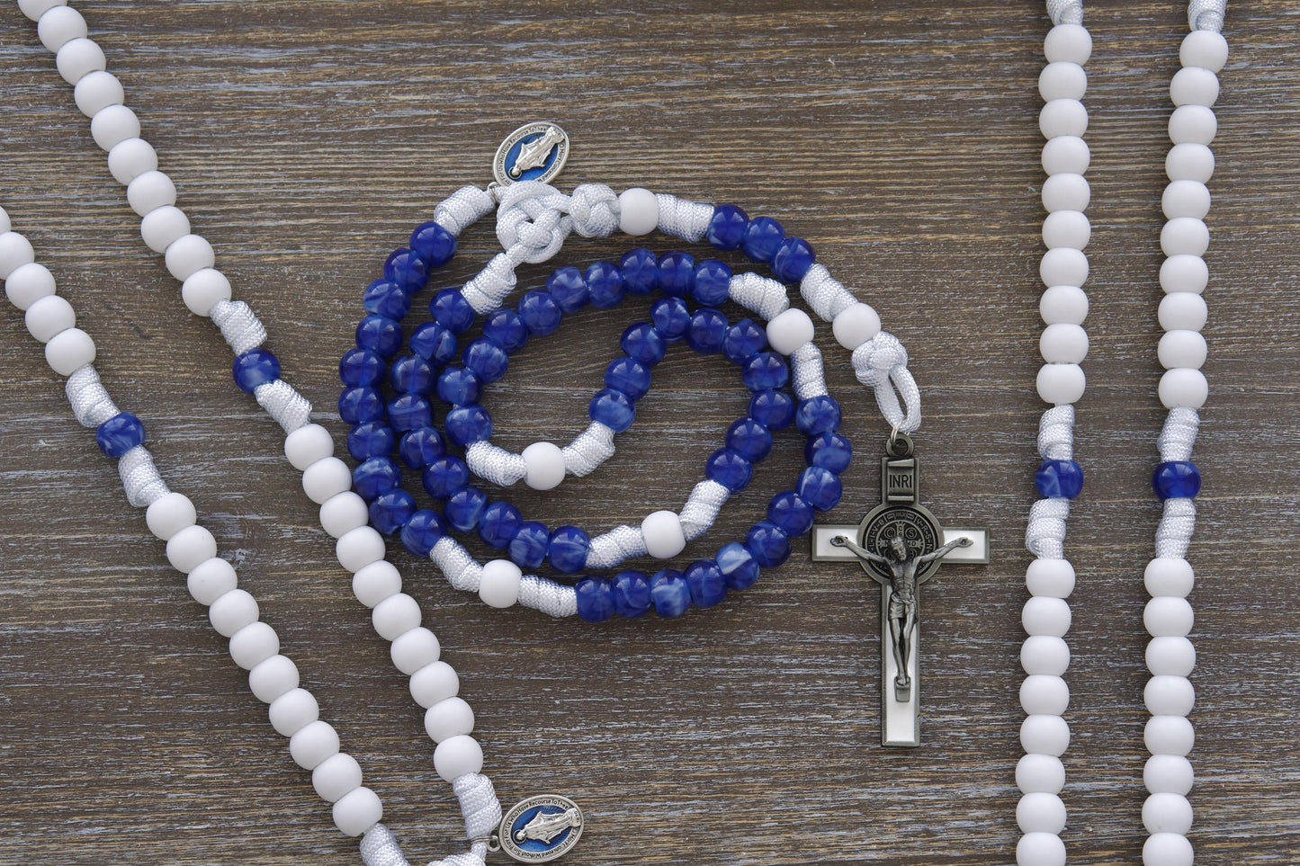 Our Lady's Mantle 5 Decade Paracord Rosary: Two stunning styles featuring white paracord, a blue enamel Miraculous Medal, and a white enamel St. Benedict crucifix. 12mm matte white and milky miraculous blue acrylic beads adorn this handmade rosary