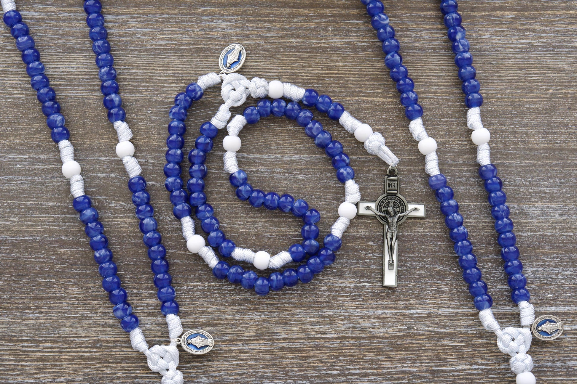 Our Lady's Mantle" 5 Decade Paracord Rosary: A handcrafted rosary featuring durable white paracord, a blue enamel Miraculous Medal, and a white enamel St. Benedict crucifix. Two distinct styles are available.