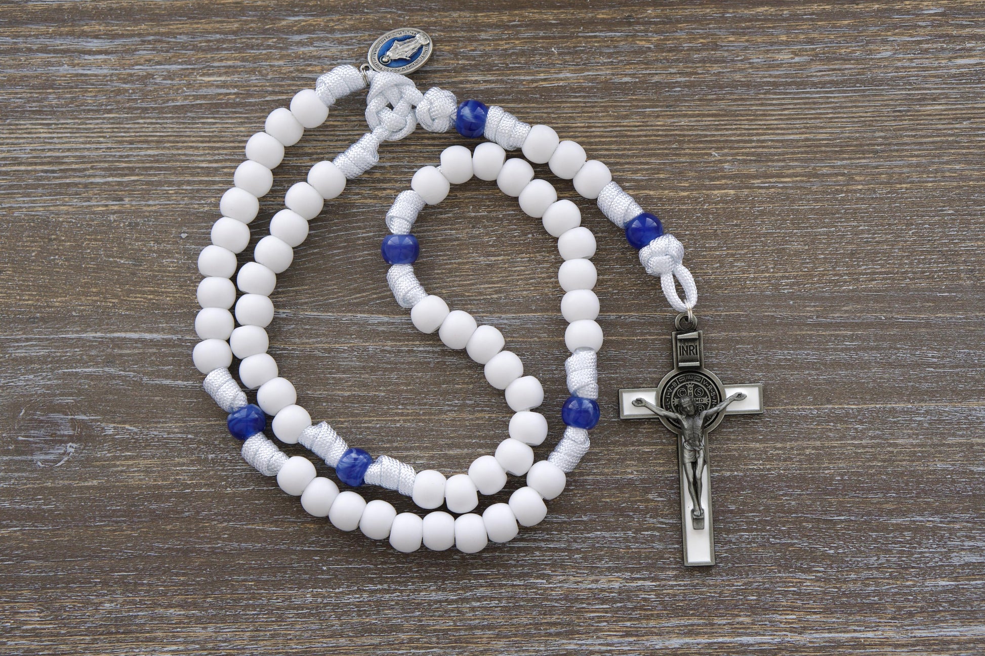 A handcrafted "Our Lady's Mantle" 5-decade paracord rosary featuring two distinct styles.  White paracord contrasts with a blue enamel Miraculous Medal and a 3-inch white enamel St. Benedict crucifix.