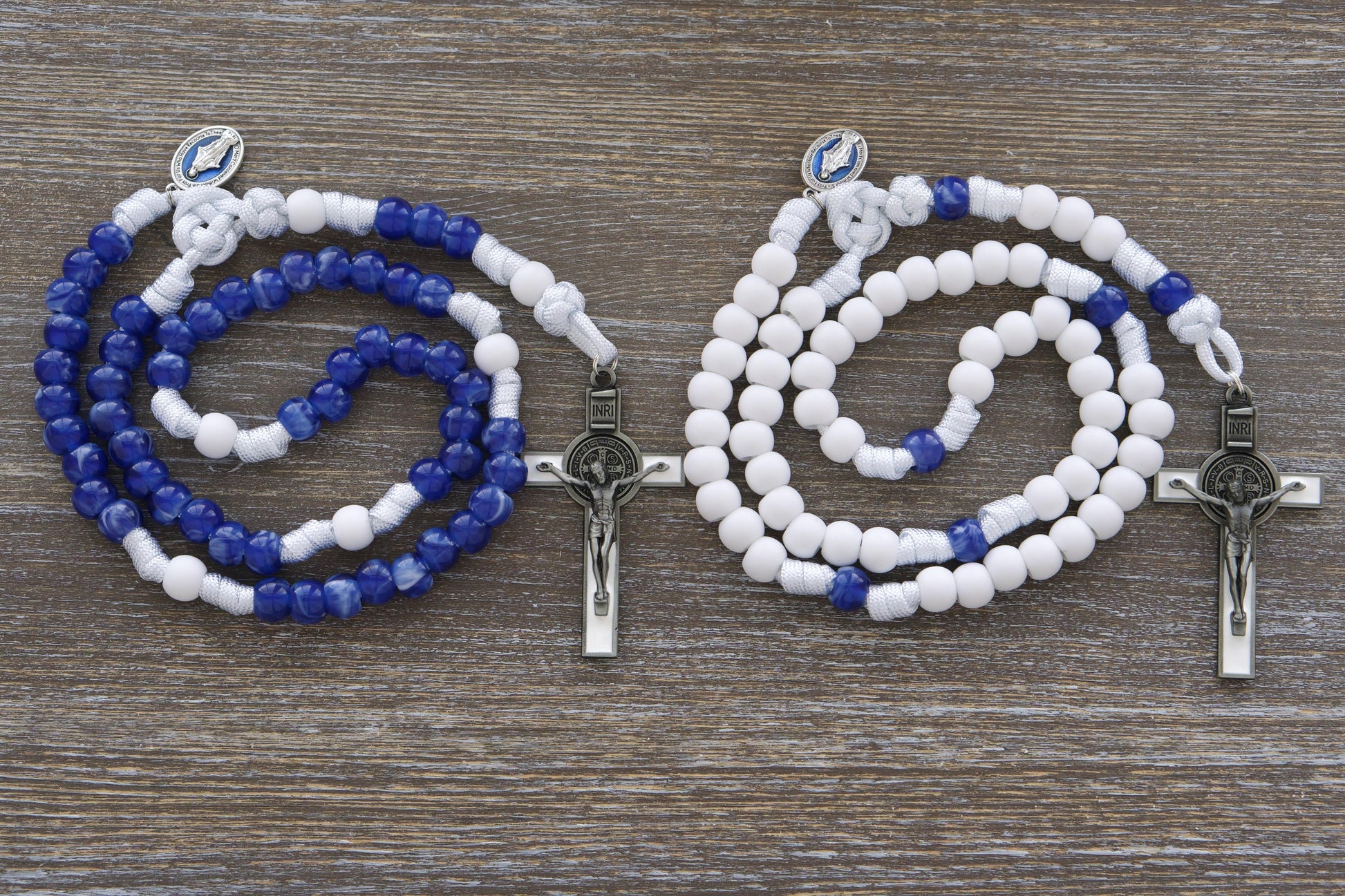 Strong white paracord rosary featuring a blue enamel Miraculous Medal and a white enamel St. Benedict crucifix. Available in two distinct styles with 12mm matte white and "miraculous blue" acrylic beads, honoring Our Lady's Mantle for spiritual protection and devotion. Handmade by Sanctus Servo.