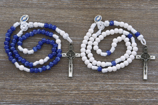 Strong white paracord rosary featuring a blue enamel Miraculous Medal and a white enamel St. Benedict crucifix. Available in two distinct styles with 12mm matte white and "miraculous blue" acrylic beads, honoring Our Lady's Mantle for spiritual protection and devotion. Handmade by Sanctus Servo.
