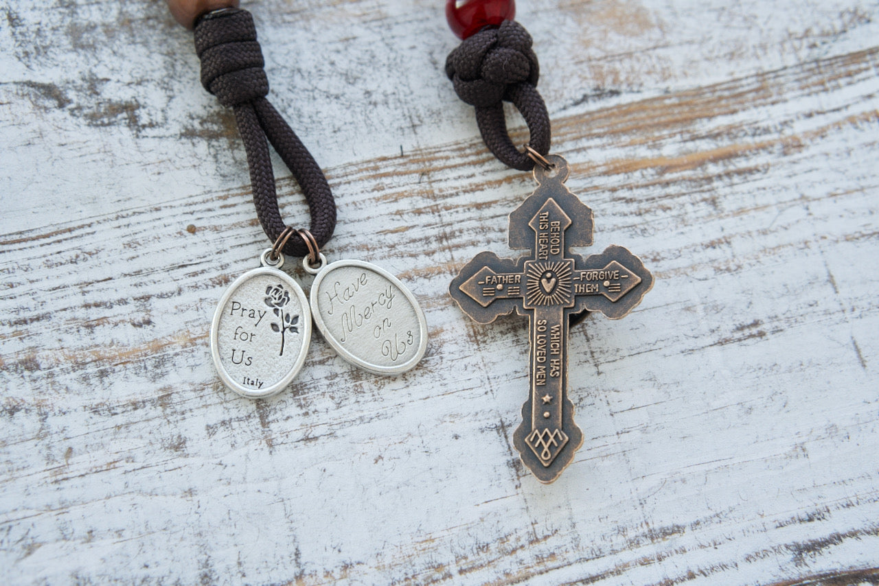 St. Padre Pio's Intercession - 1 Decade Paracord Rosary: A beautifully designed, durable paracord rosary honoring St. Padre Pio with antique copper Hail Mary beads, deep maroon Our Father bead for the Stigmata, devotional medals for St. Padre Pio and Sacred Heart of Jesus, and a standard size copper Pardon Crucifix. Perfect for deepening faith and as a Catholic gift.