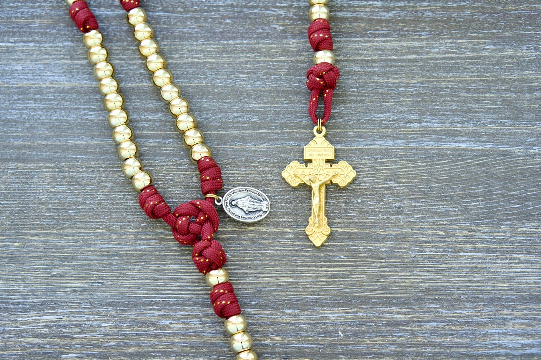 Kid's 5 Decade Paracord Rosary 'Scarlet Crown', featuring 10mm gold beads, red paracord with a gold ribbon, golden Hail Mary and Our Father beads, gold Pardon Crucifix, Miraculous Medal, and handmade by Sanctus Servo.