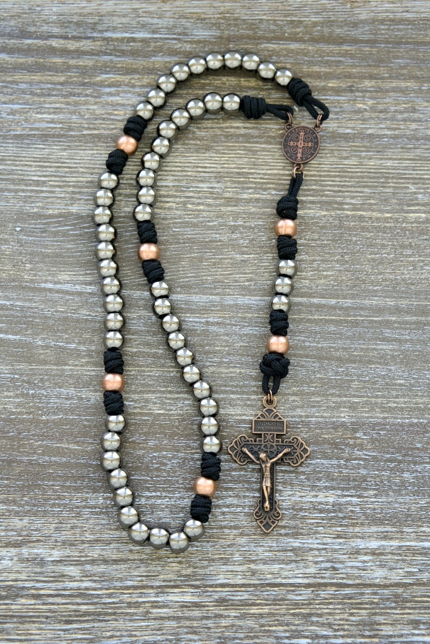 Path of the Disciple - Premium Metal Paracord Rosary: A robust and sleek black paracord rosary, featuring gunmetal Hail Mary beads and antique copper Our Father beads for a visually pleasing and spiritually resonant design. This handmade rosary with metal alloy beads includes a St. Benedict medal centerpiece and 2 inch Pardon crucifix, perfect for deepening your connection to the Catholic faith and walking the path of discipleship.