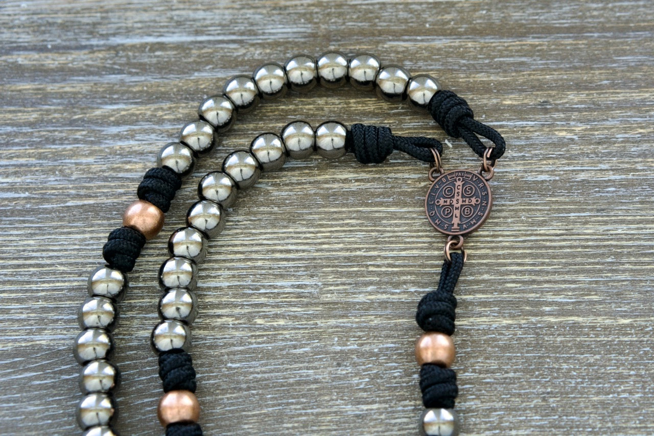 Path of the Disciple - Premium Metal Paracord Rosary, handmade by Sanctus Servo for Catholic devotionals; featuring black paracord 275, gunmetal Hail Mary beads, antique copper Our Father beads, St. Benedict medal centerpiece, and 2 inch Pardon crucifix for a spiritually resonant and durable rosary accessory.
